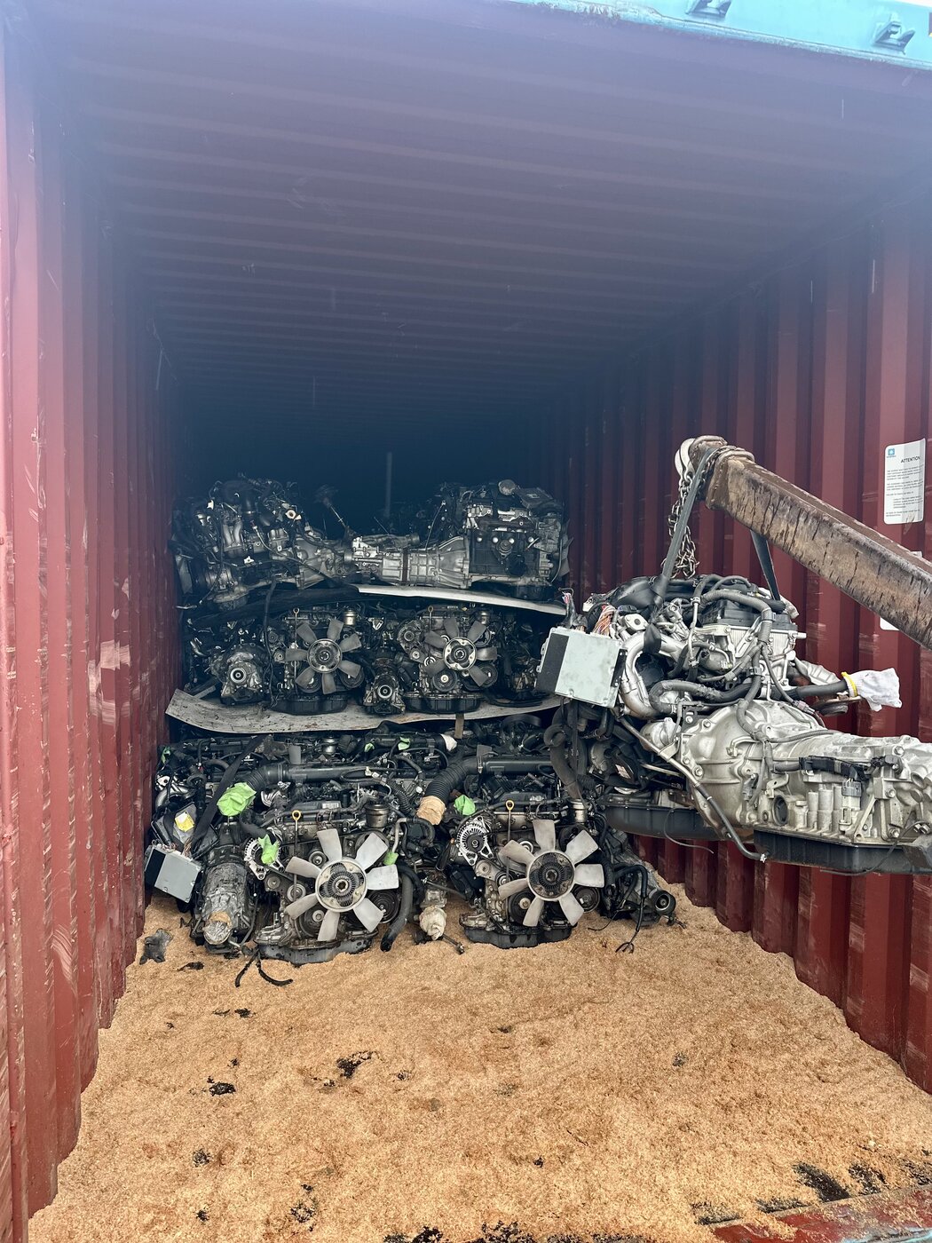 Engine and transmission being lifted into a container stacked with engines