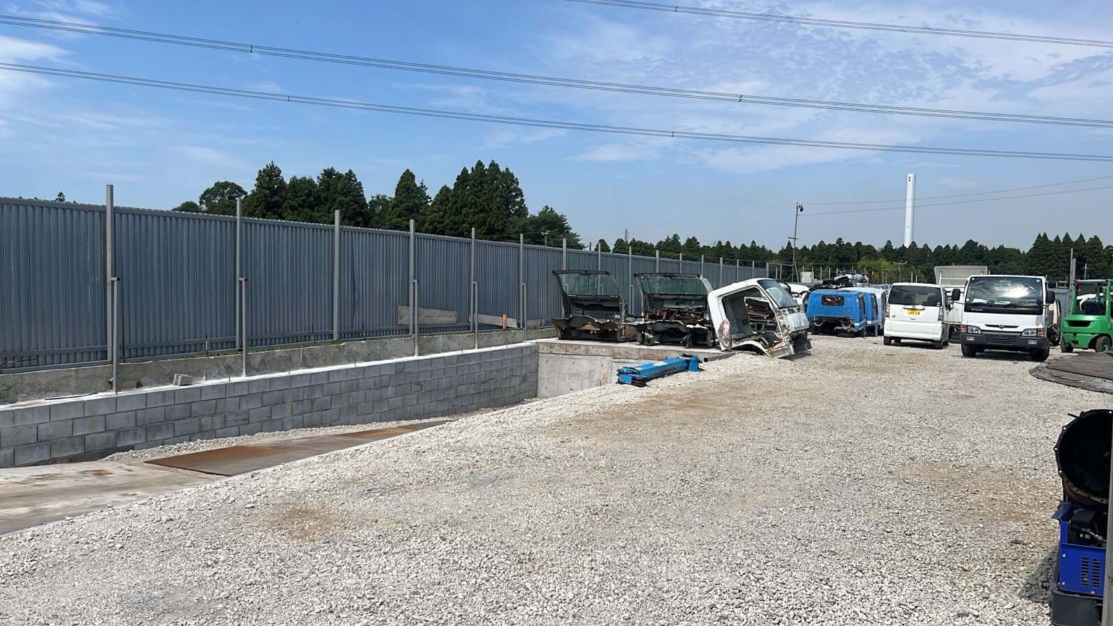 Gotencho Vehicle Storage Yard — gravel yard with loading area, vehicle cabs, parked trucks and a forklift