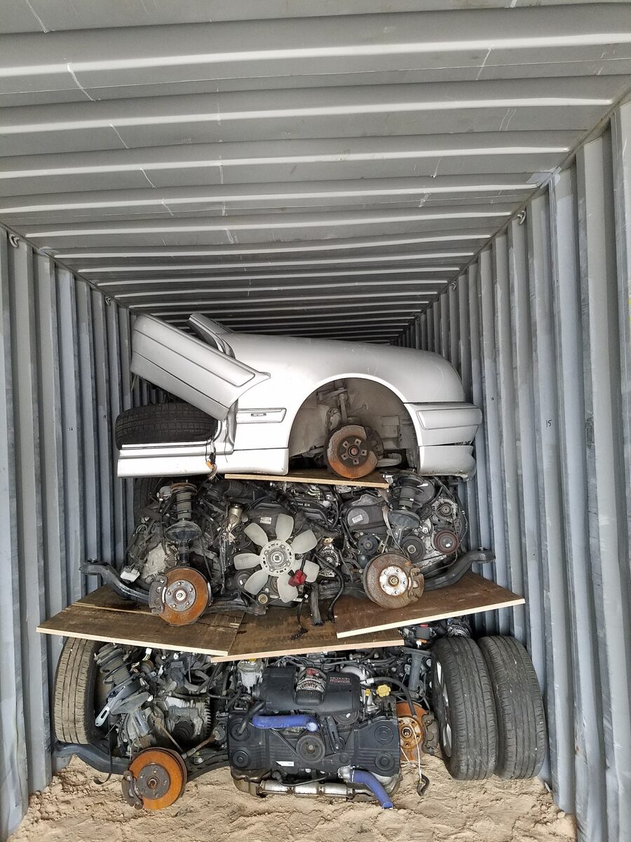 White vehicle front section stacked above engines inside a container