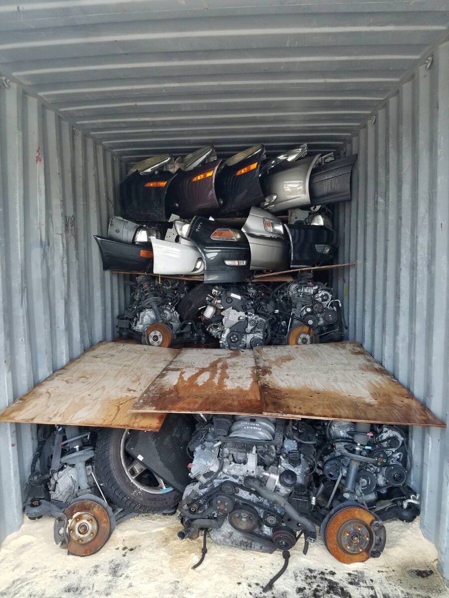 Vehicle panels stacked behind a wooden loading platform inside a container