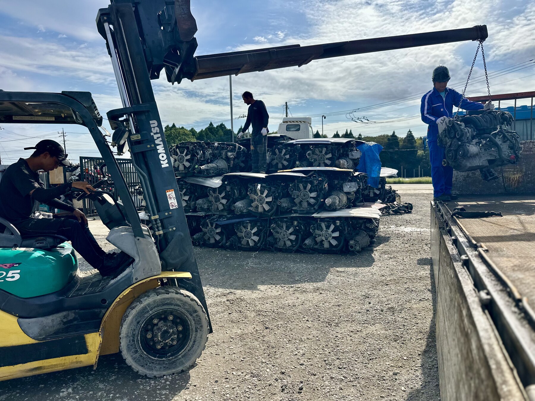 Forklift beside stacked engines and workers in the yard