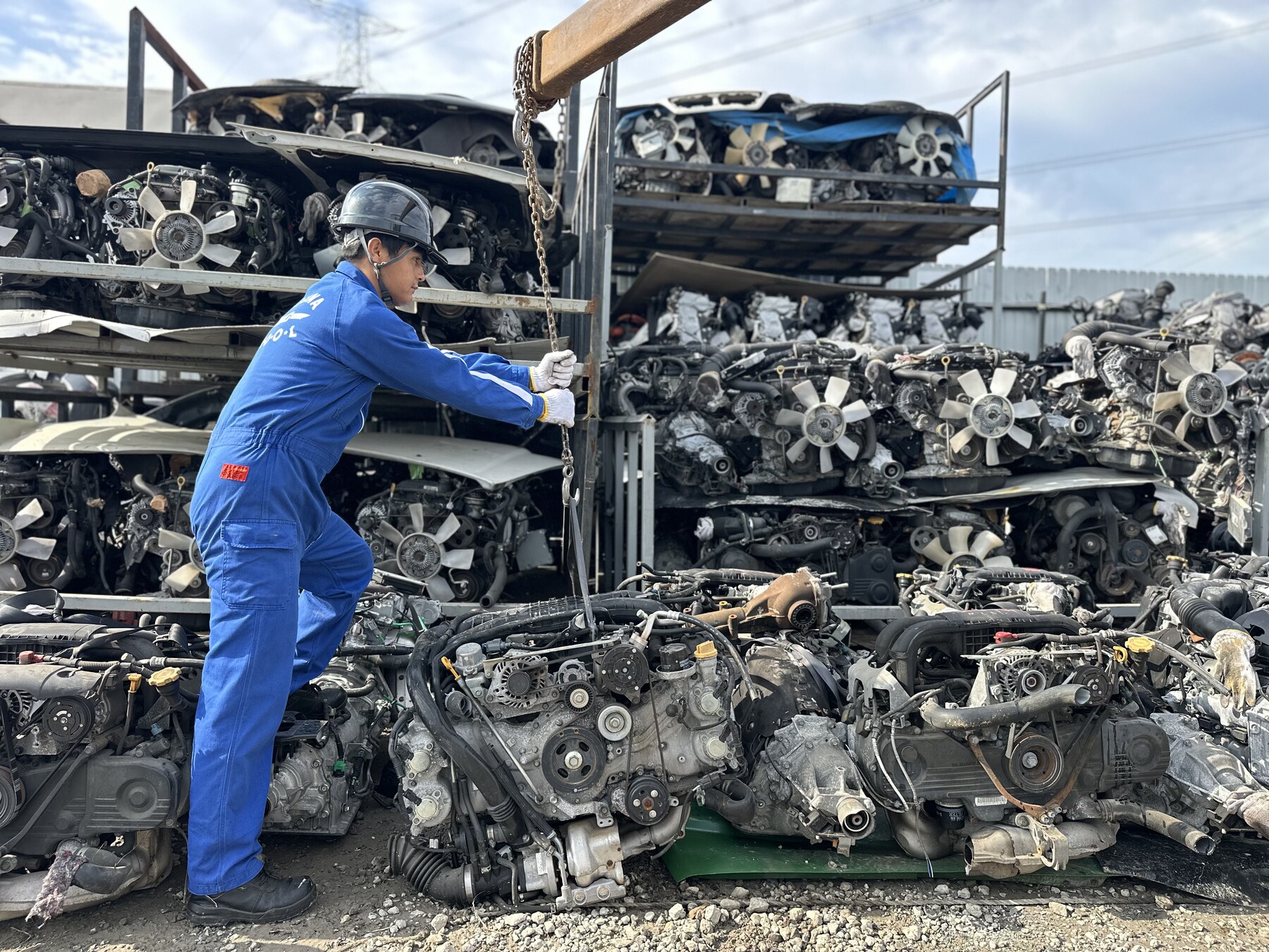 Worker handling an engine beside stocked engine racks